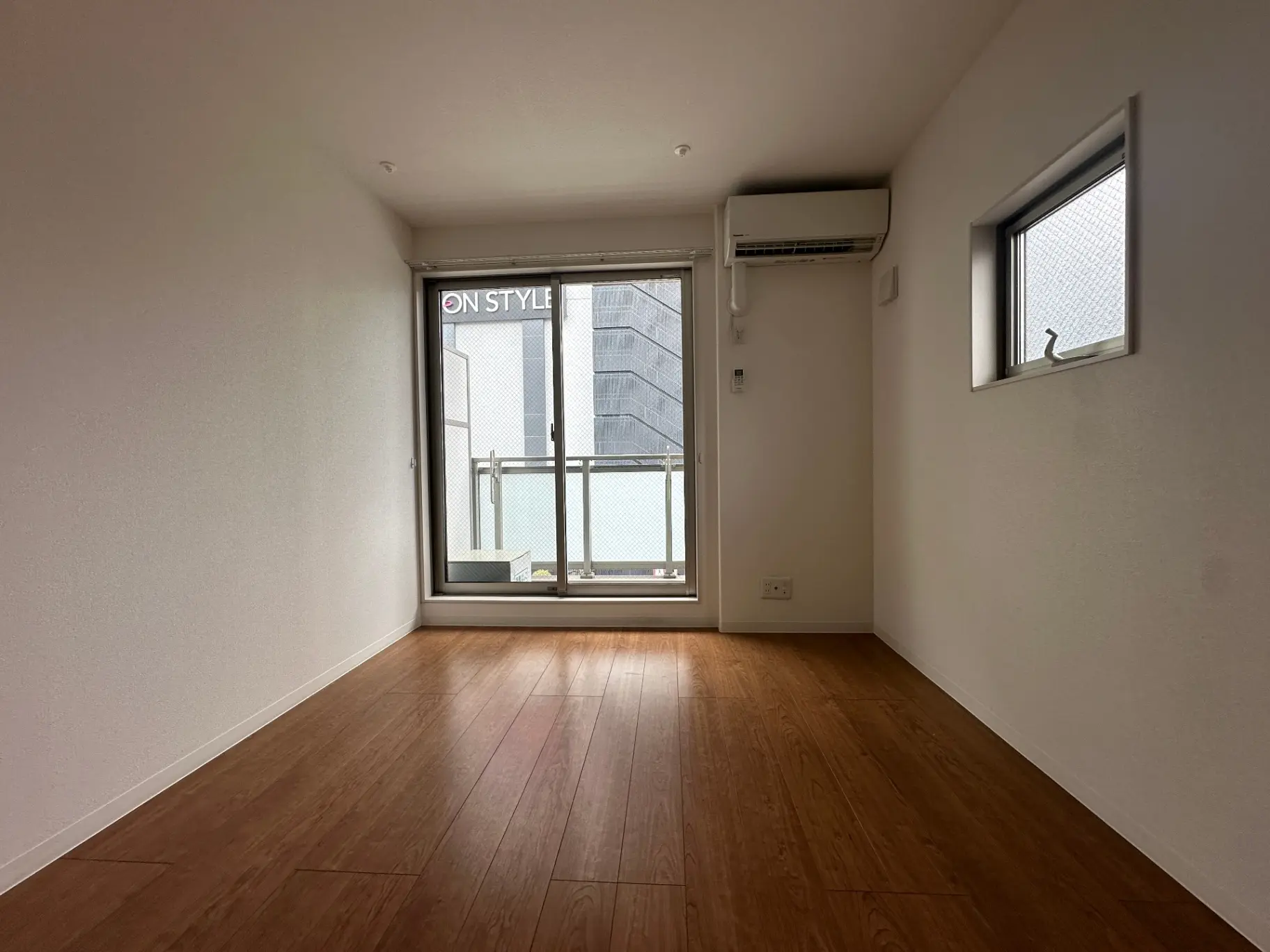 シンプルで広々とした空き部屋、木目調のフローリング、大きなガラス窓と室内照明設備が備わったインテリア