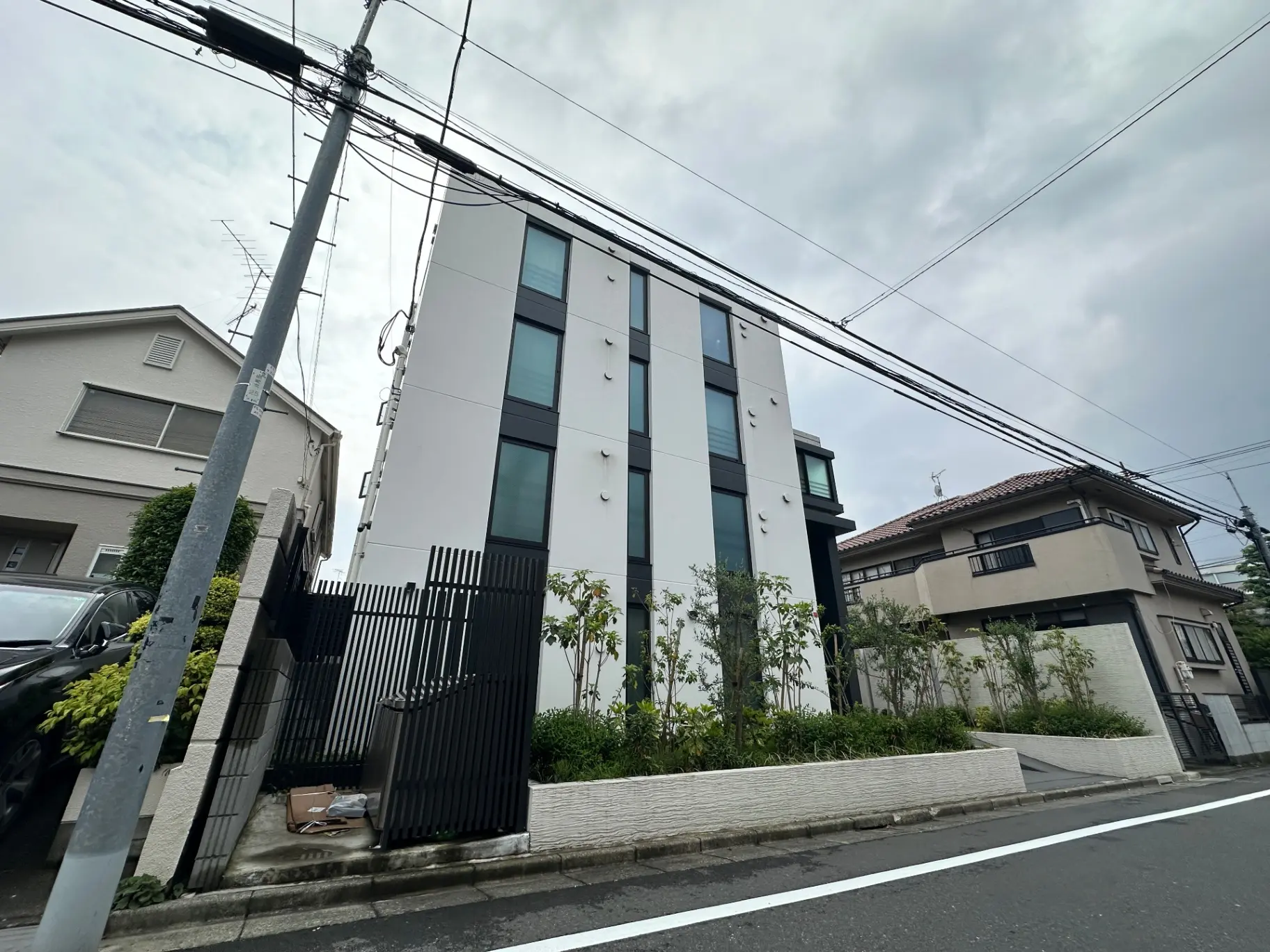 都市の住宅街にあるモダンなデザインの白い建物と伝統的な日本家屋、道路沿いの風景