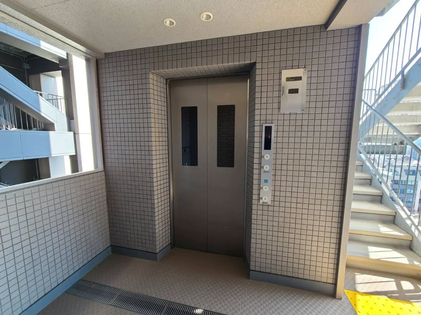 タイル張りのエレベーターエントランス、自然光が差し込む階段