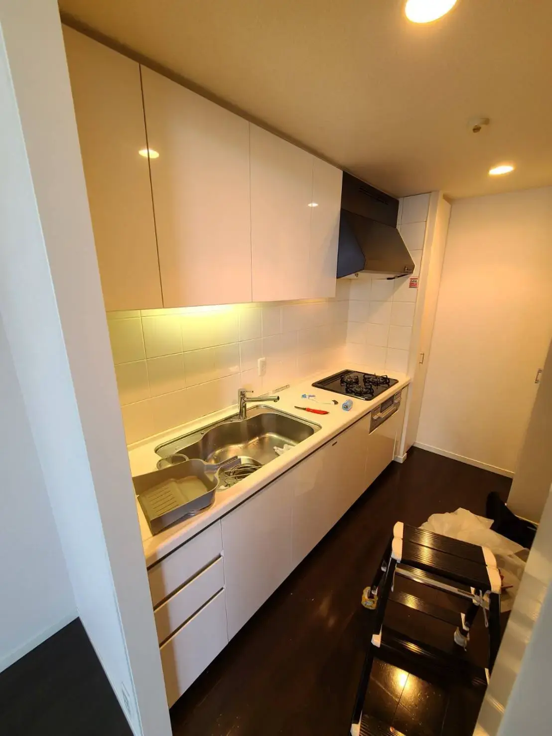 コンパクトなキッチン、ホワイトキャビネット、ダークブラウンのフローリング、組み込みガスコンロとシンク