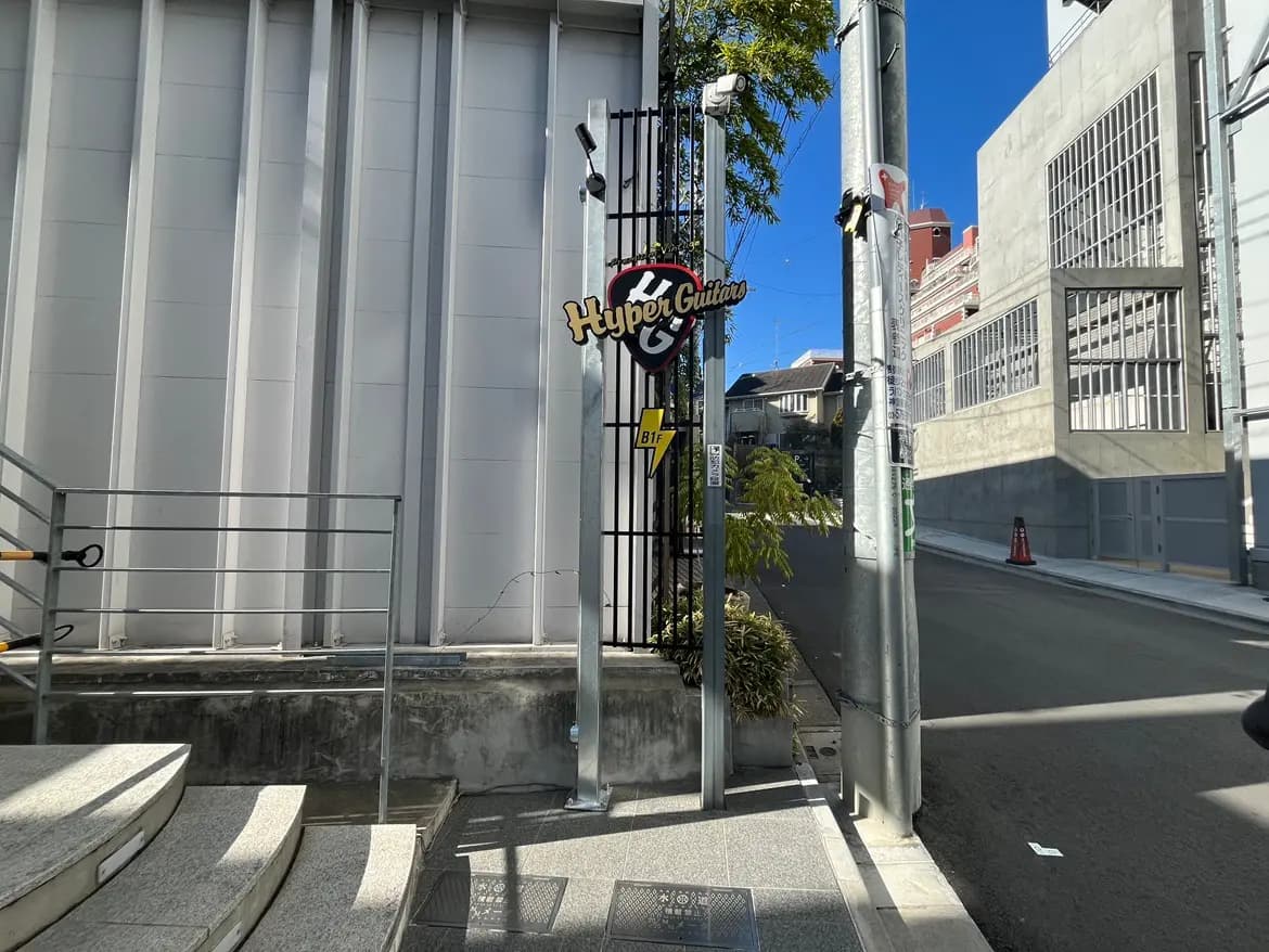 都市の日当たりの良い通りにあるHyper Guitarsの看板、コンクリートの階段と現代的な建築