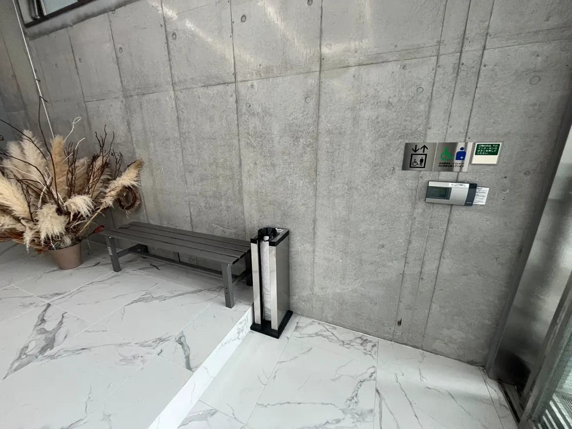現代的な建物のエントリーエリア、コンクリートの壁、待合用ベンチ、草花の装飾、温度管理システム