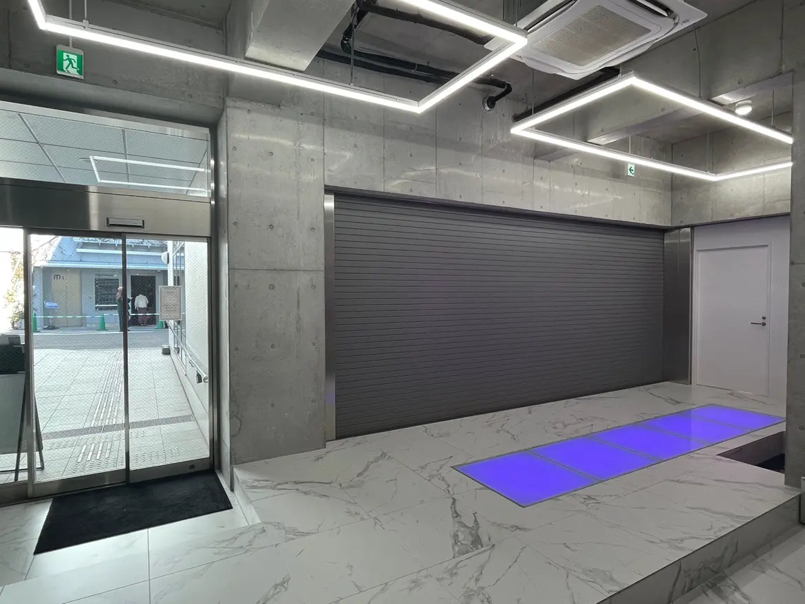 現代的なオフィスエントランス、コンクリートと大理石の壁、特徴的なLED照明、自動ガラスドア