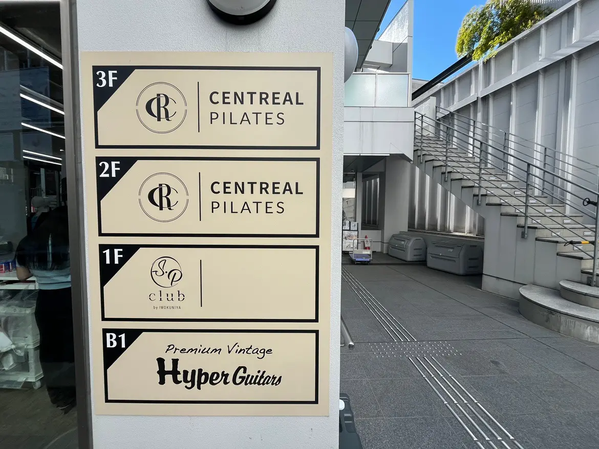 建物の案内看板、ピラティススタジオとヴィンテージギターショップのロゴがある看板