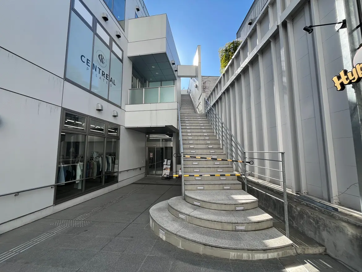 都会のモダンな建物入り口と屋外階段、ガラス扉と白い壁、日差しが照りつけるクリアな天気