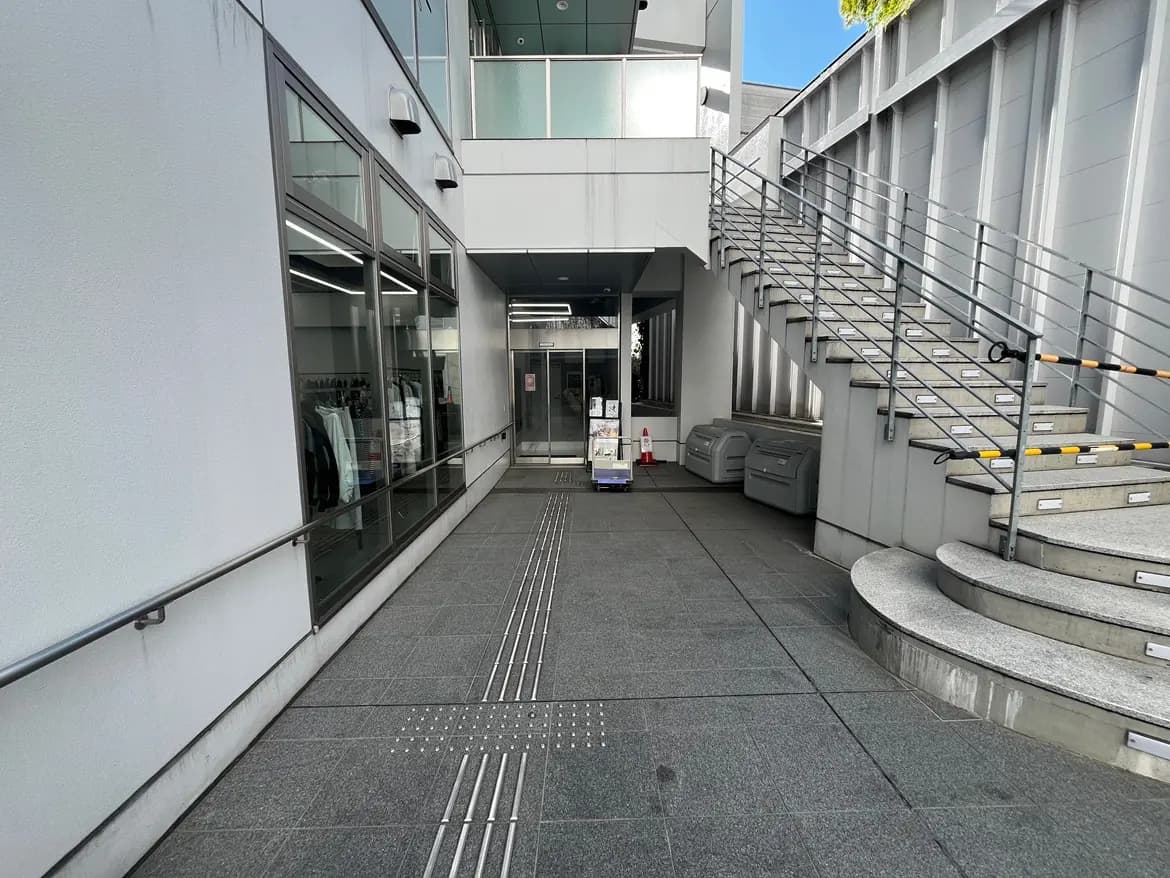 現代的なオフィスビルのエントランス、ガラス扉、灰色のタイル床、螺旋階段と案内標識のある都市の建築デザイン