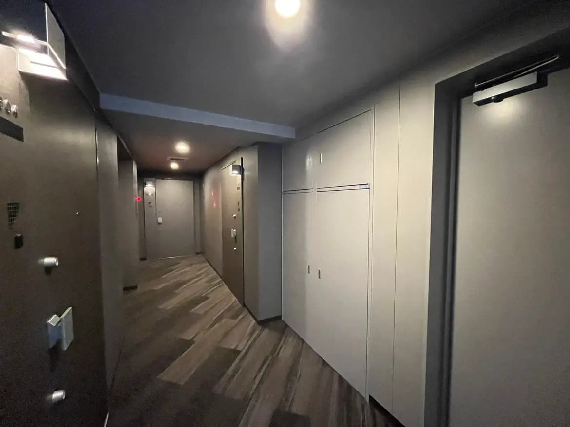 モダンなマンションの廊下、木目調のフローリング、白い壁とドア、LED照明
