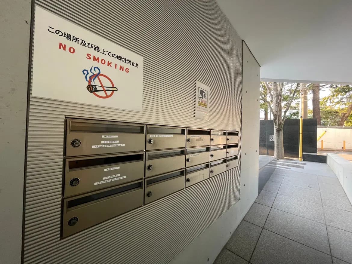 禁煙サインが掲示されたマンションのエントランスホール、メタル製の郵便受けが壁に埋め込まれている