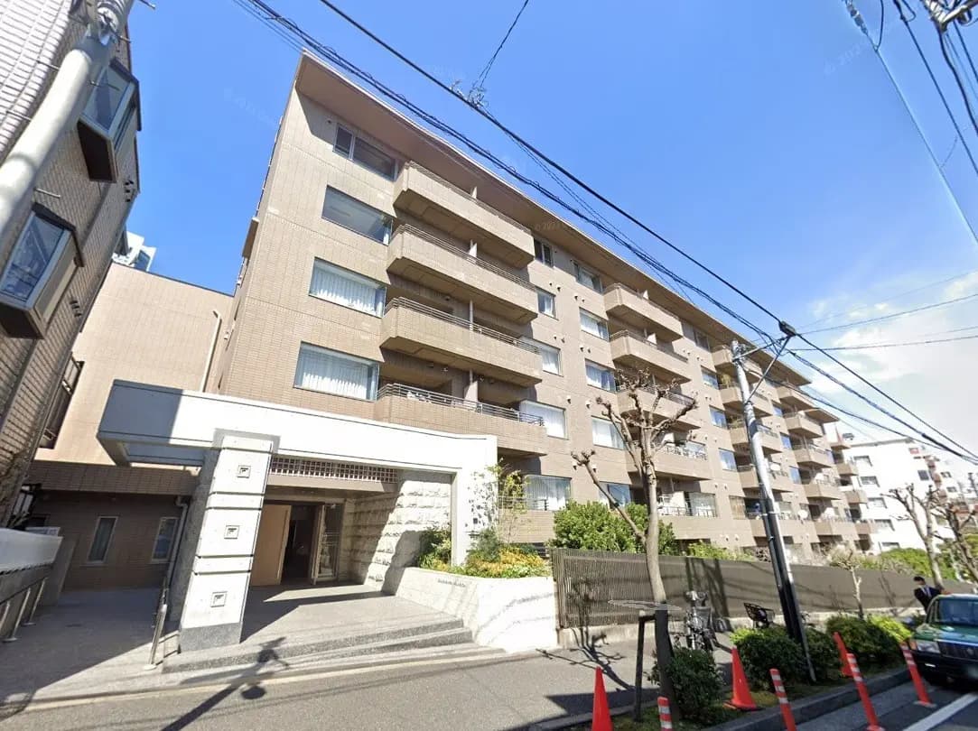 都市部のモダンなマンション外観、エントランス付近の植え込みと広い歩道