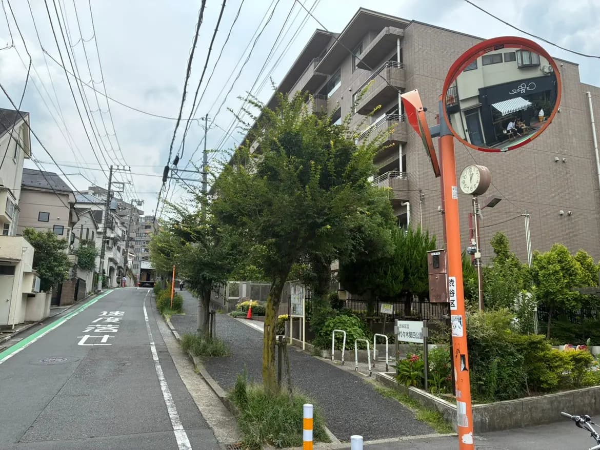 - 街の風景、傾斜のある道路と緑の植栽、マンションの外観、道路標識とミラーが映る情景