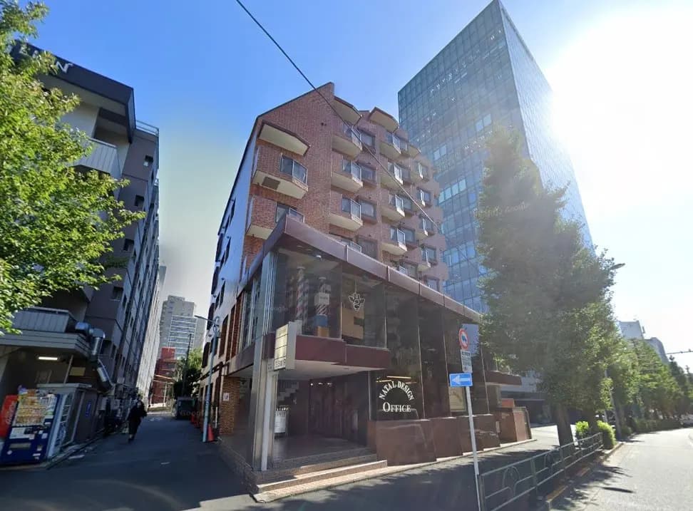 都市の通り角にあるレンガ造りのビルとガラス張りの高層ビル、晴れた日の青空と周囲の緑が映える景観