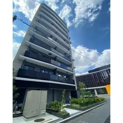 - 現代的なデザインのマンション外観、青空と白い雲を背景にした6階建ての建物、緑豊かなエントランスの風景
