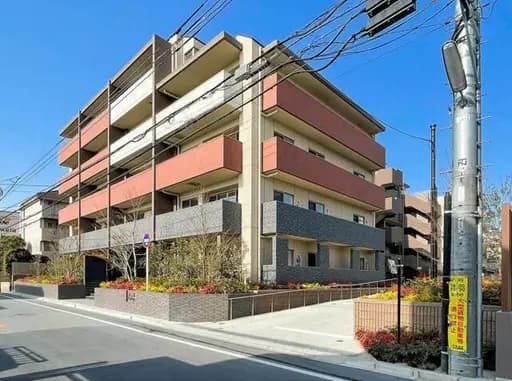 - モダンなデザインのマンション外観、三階建ての建物と整備された植栽、青空の下にある風景