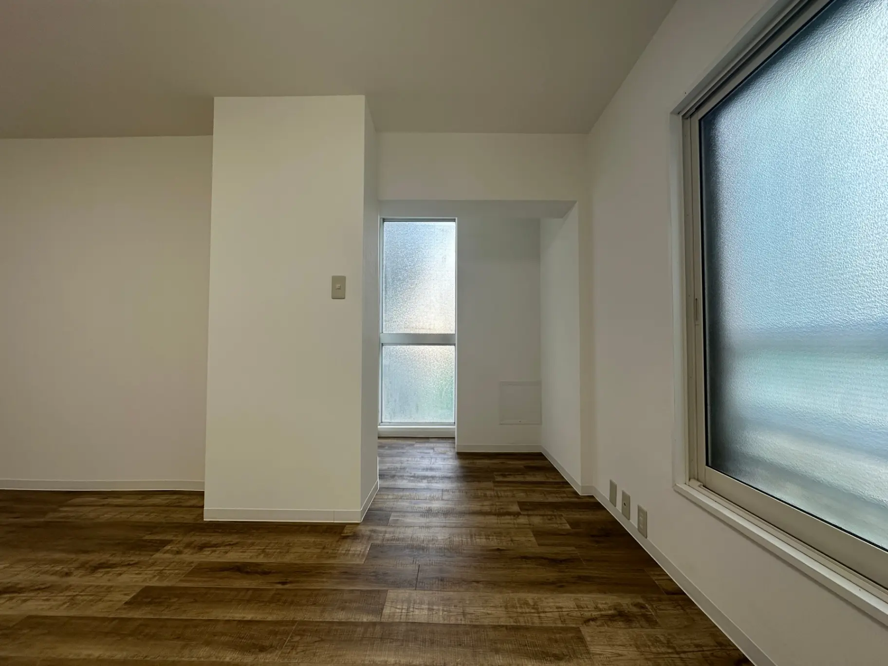 シンプルなデザインの新築マンションの部屋、木目調フローリング、大きな窓から採光を取り入れた明るい空間