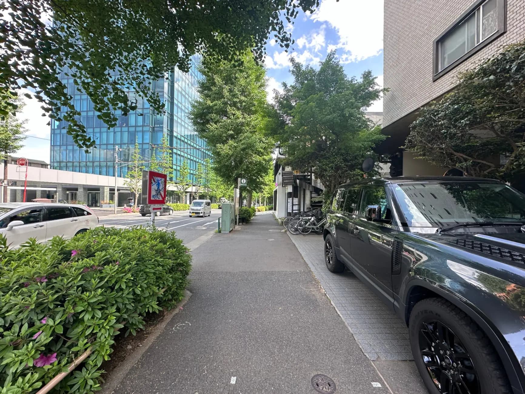都会の街路沿いに停車している高級SUV車、背景にはガラス張りのオフィスビルと緑豊かな樹木