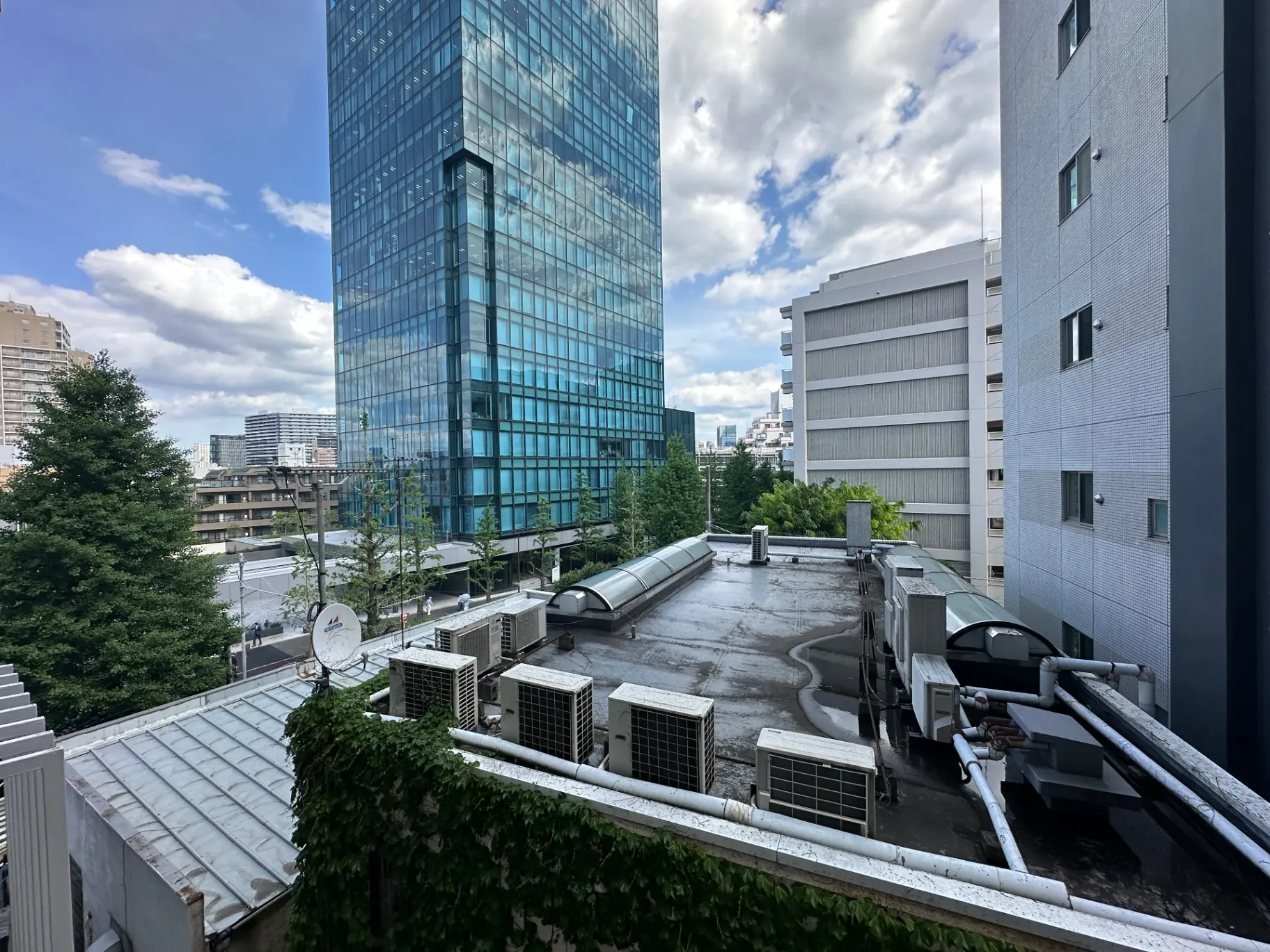 都市の建物と屋上、駐車場と緑豊かな木々が見える景観