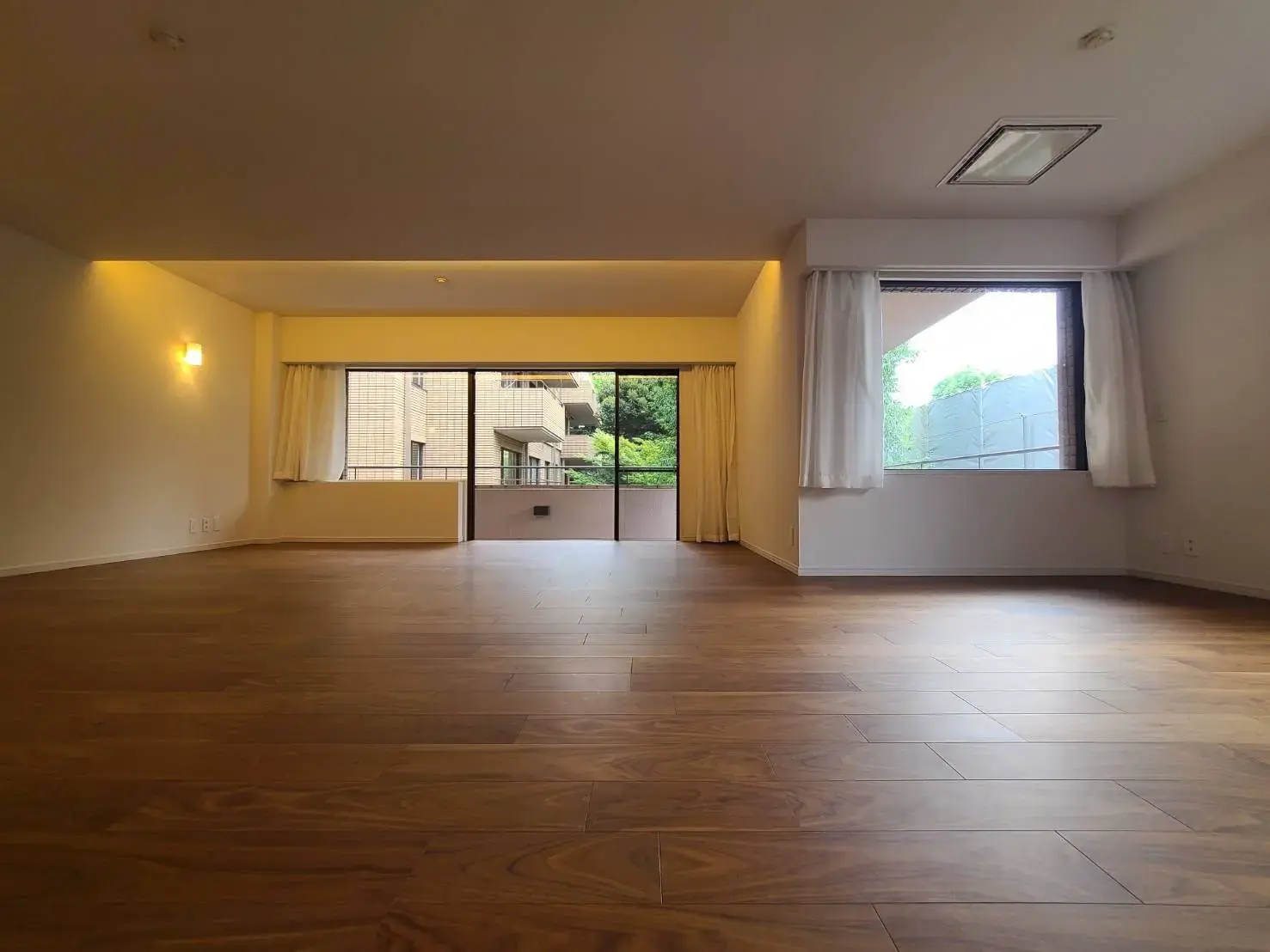 広々とした空間と木製フローリングが特徴のリビングルーム、自然光が差し込む大きな窓とやわらかな照明