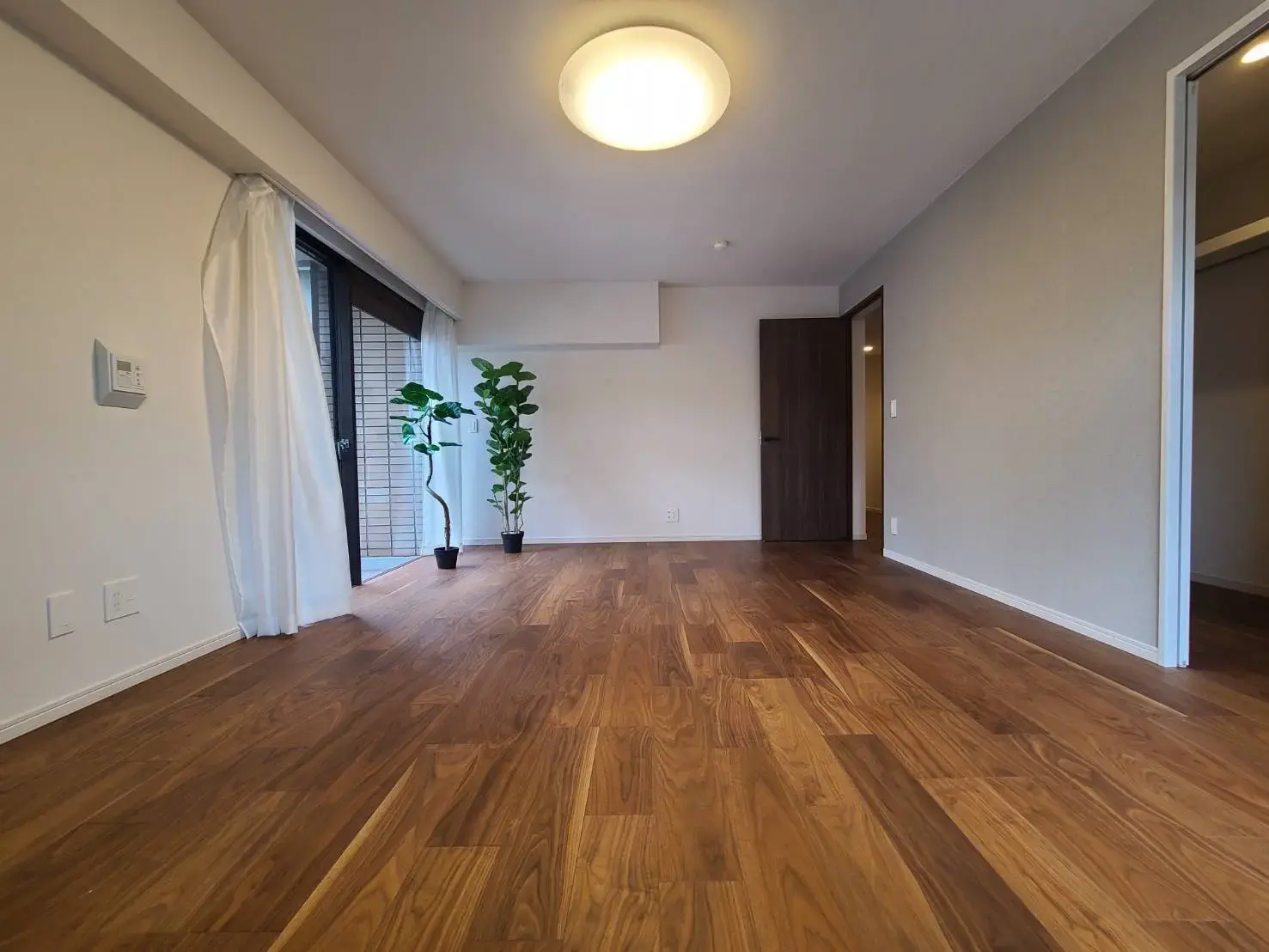 シンプルで洗練されたデザインの空き部屋、木目調のフローリング、ガラスドア付きの明るいバルコニーへのアクセス