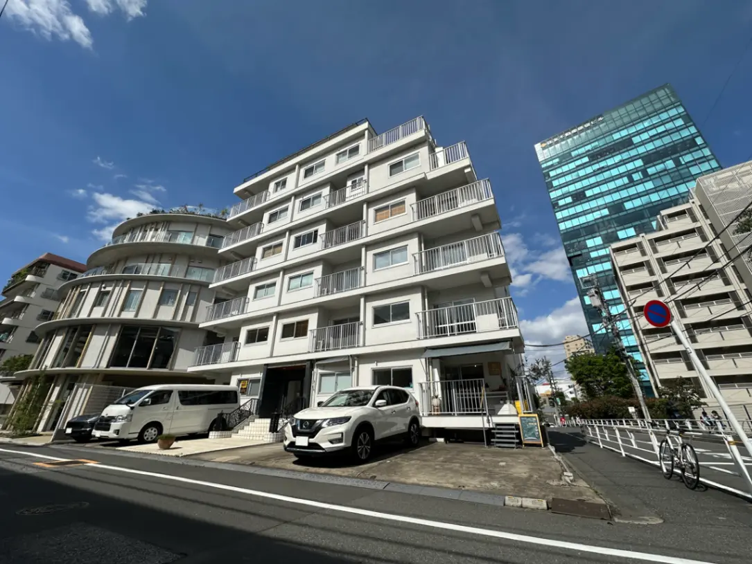 都市の住宅街にあるモダンなマンション、駐車場付き、青空と高層ビルの背景