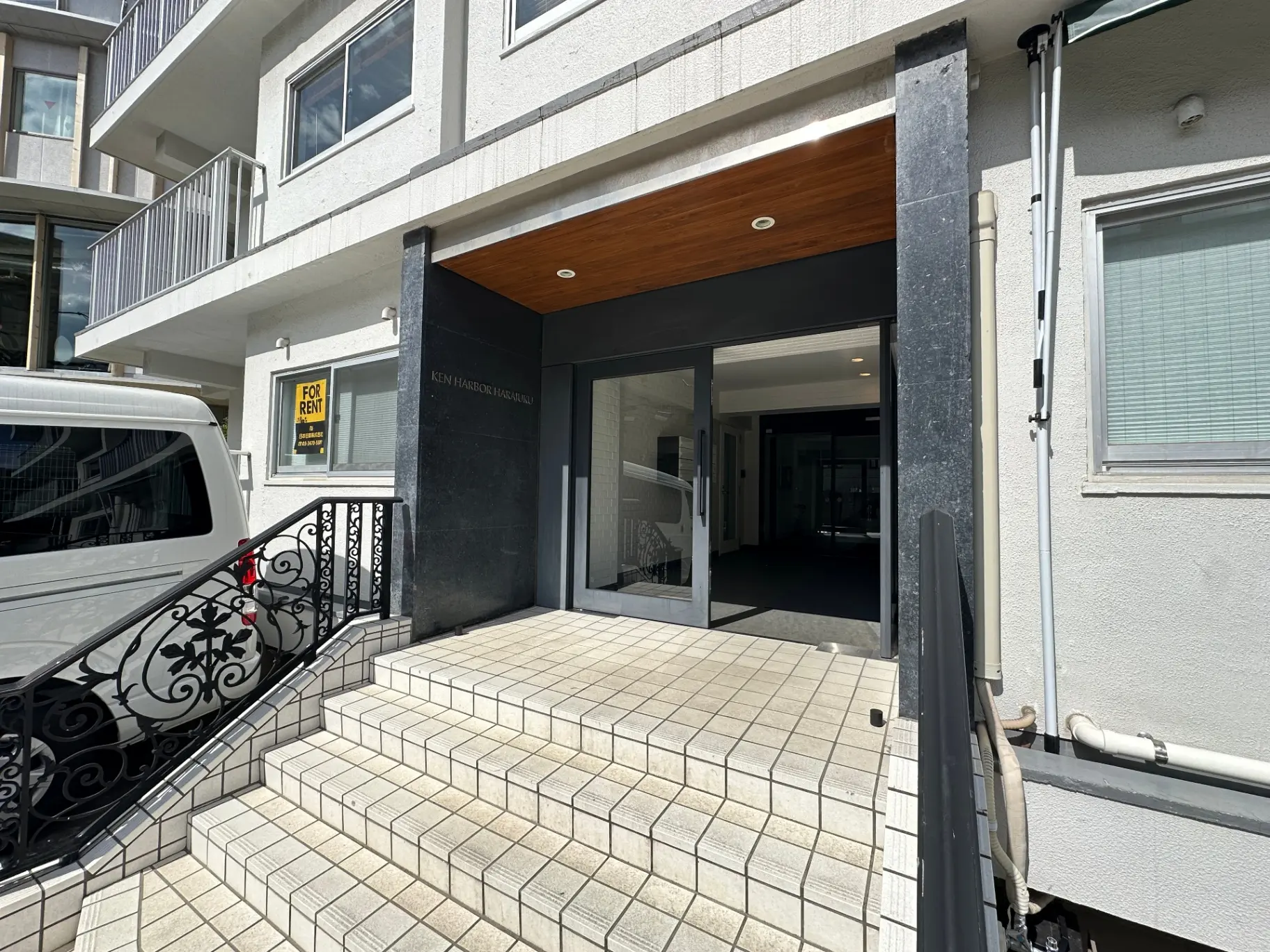 賃貸物件の入り口、階段と黒い手すり、ケンハーバー原宿の看板がある外観