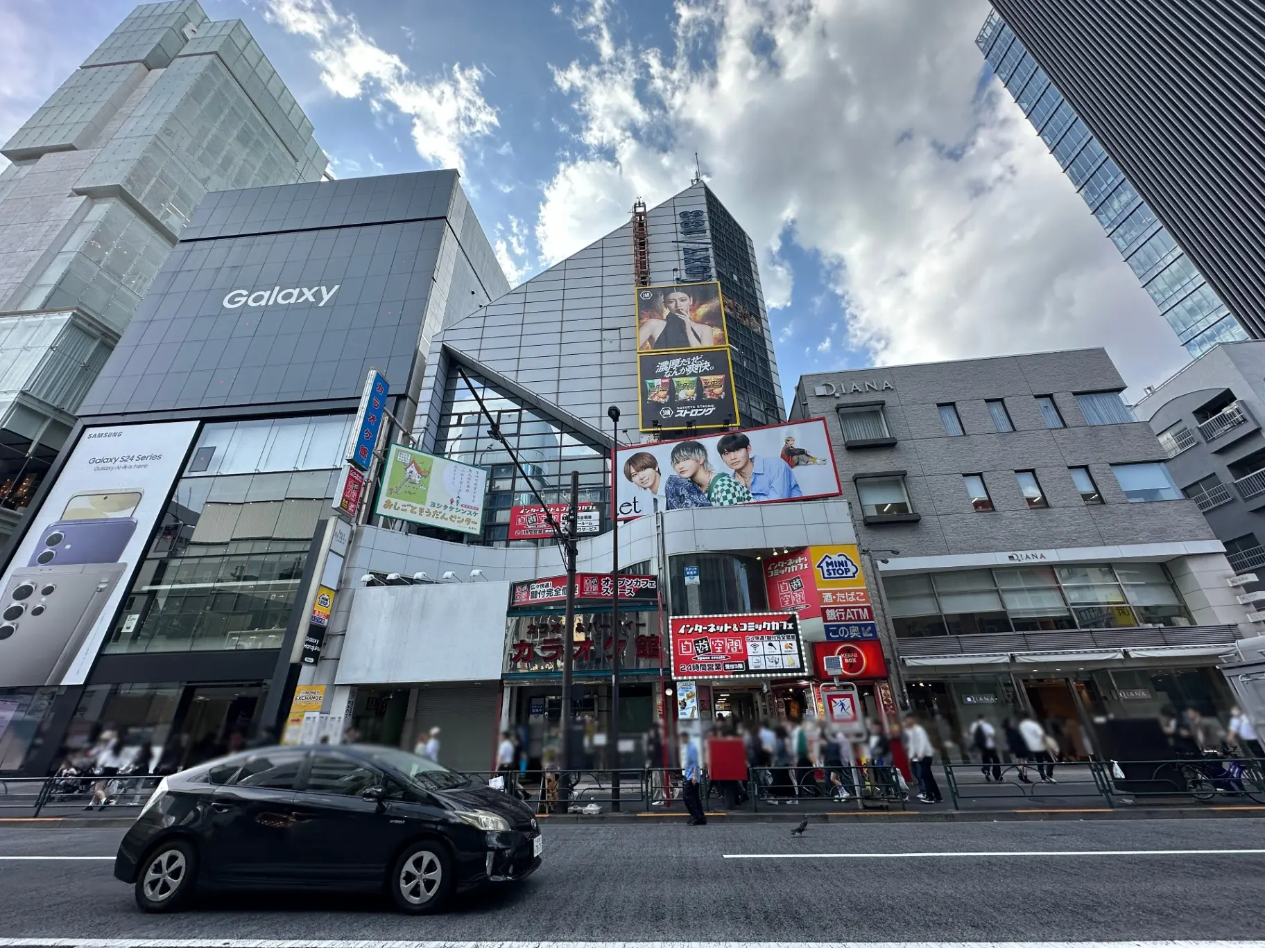 交差点の角にあるGalaxyの看板があるビルと人々で賑わう歩道、都会の風景