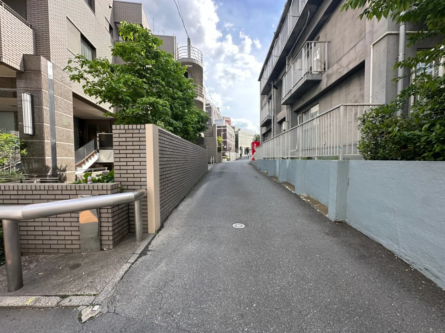 静かな住宅街の道路、アパートの建物と緑豊かな植栽が見える風景