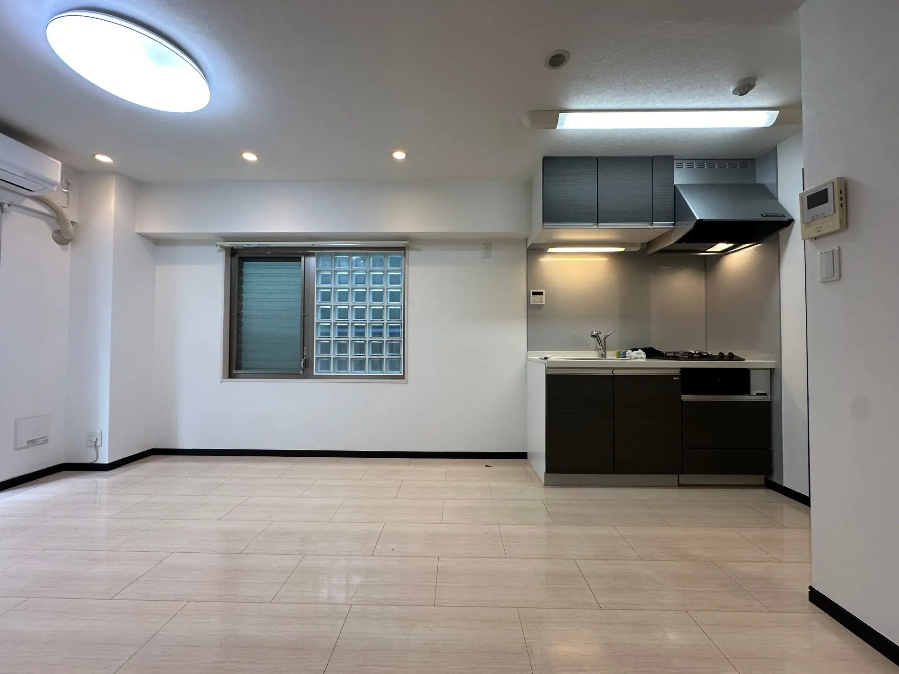 スタイリッシュなキッチン付きの広々とした白いリビングルーム、木目調のフローリング、LED照明が特徴的なインテリア