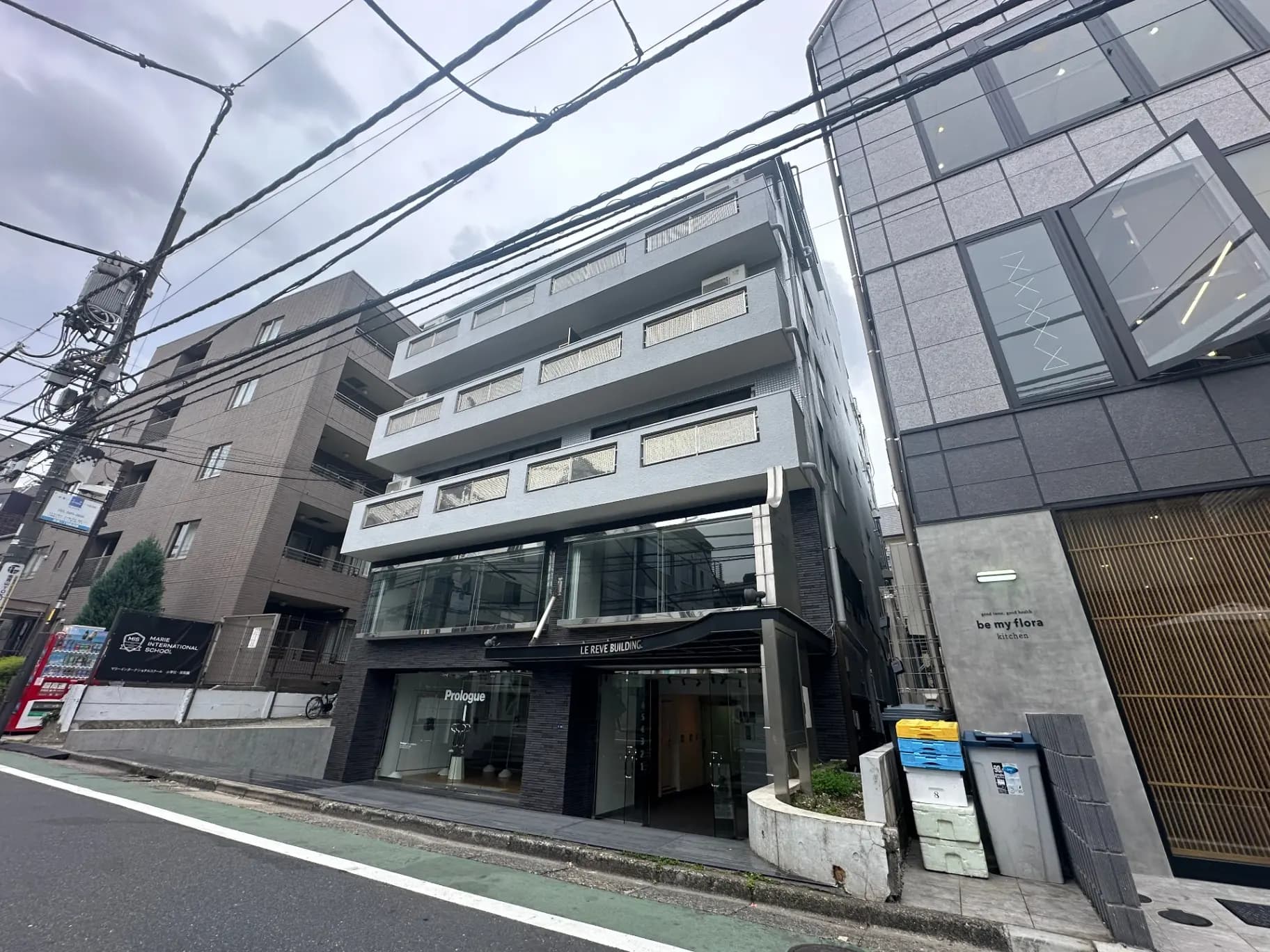 都市部に位置するモダンなデザインのマンション外観、ガラス張りの入り口と1階の店舗、電線が交差する街並み