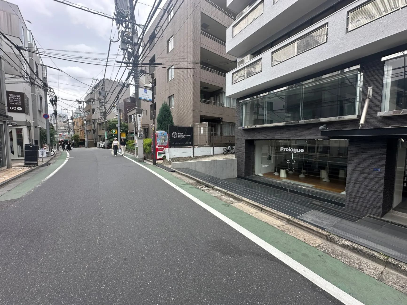 都会の住宅街の通り、黒いタイル張りの建物とショーウィンドウ、歩道に人が歩いている風景