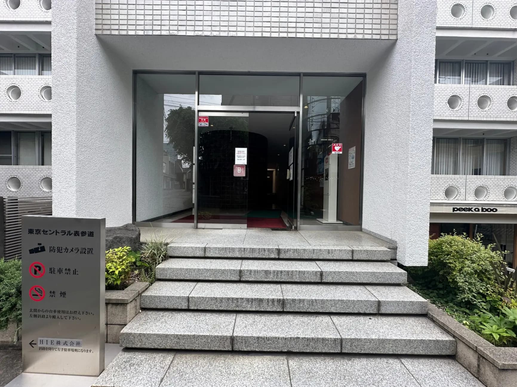 都会のオフィスビル入り口、ガラス扉と石造りの階段、植栽付き看板