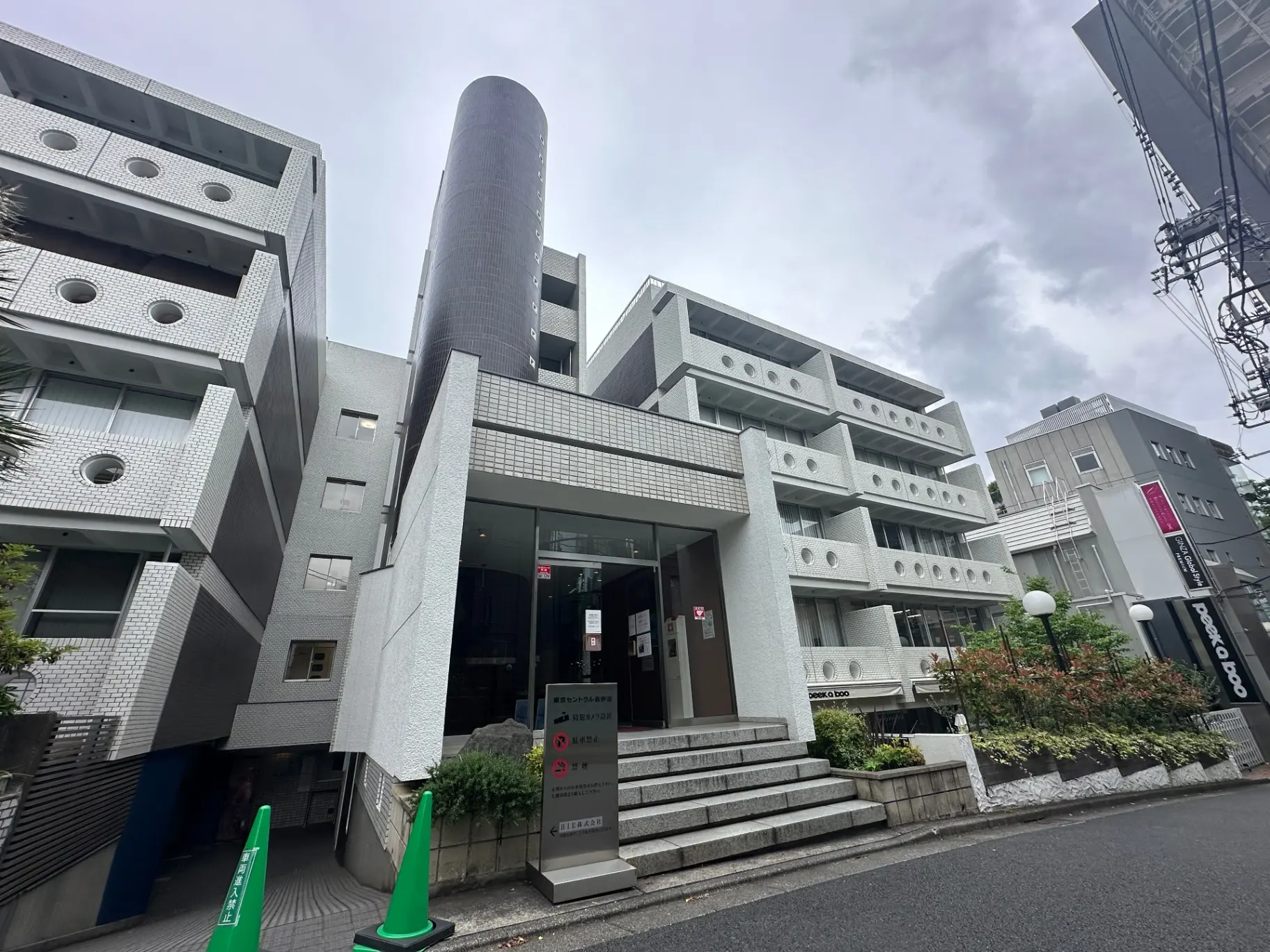 都会的な外観のマンションエントランス、白いタイル壁と円筒形の煙突が特徴的な建築デザイン