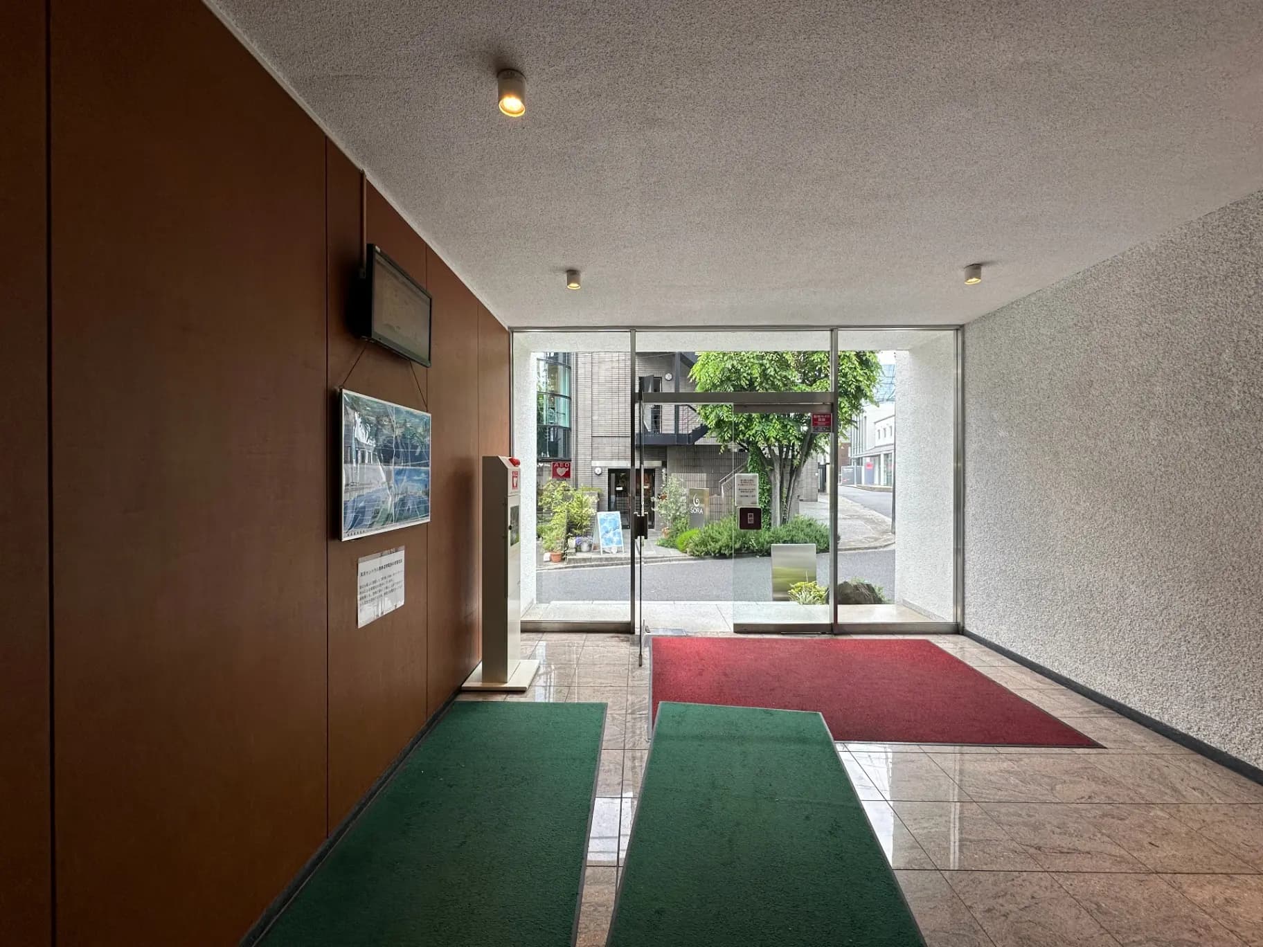 エントランスホールの内側から外の街並みを見る、床は大理石、壁には写真と案内板が掲示されたモダンなデザイン