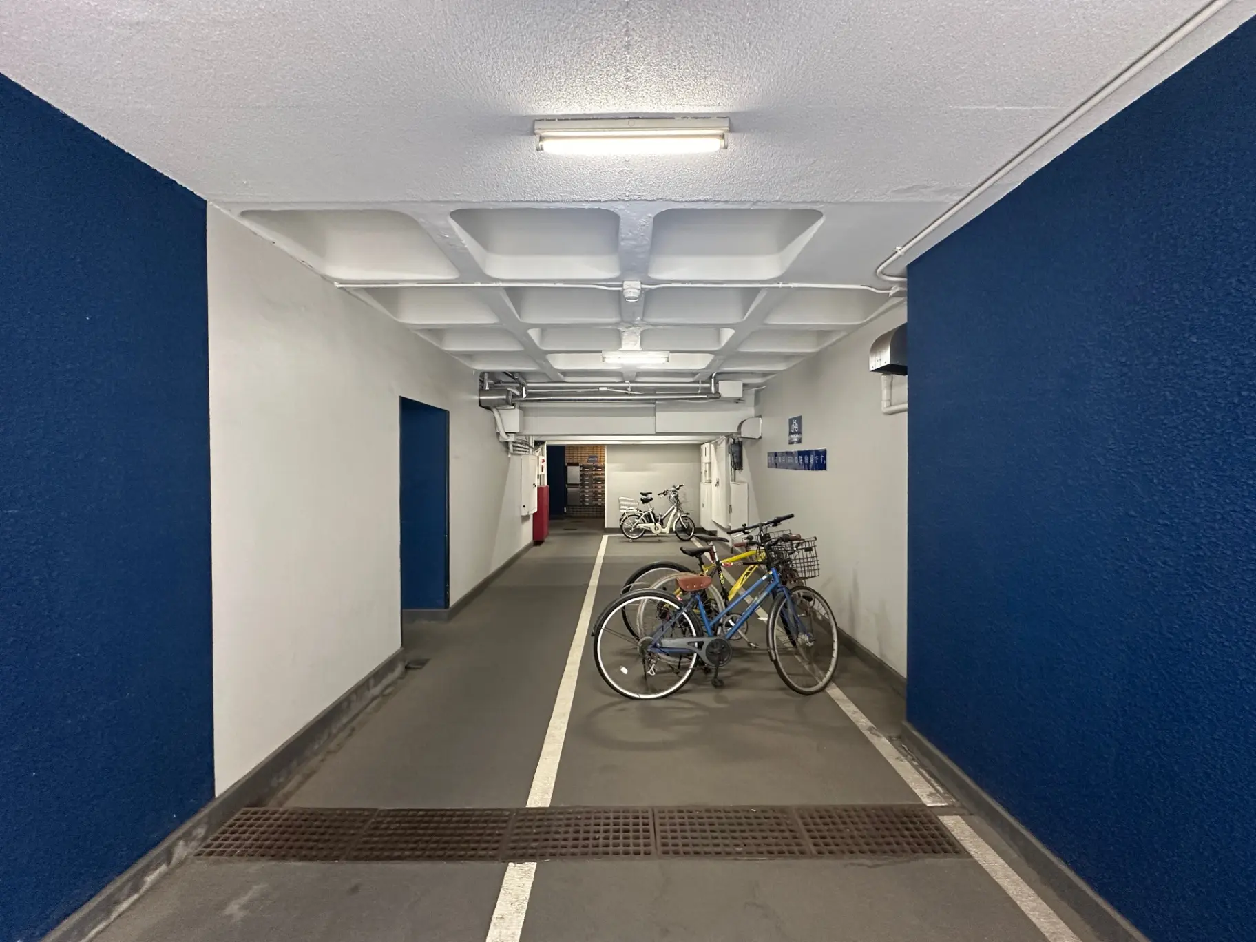 清潔で広々としたマンションの地下駐輪場、ブルーの壁と明るい照明、自転車が停められている