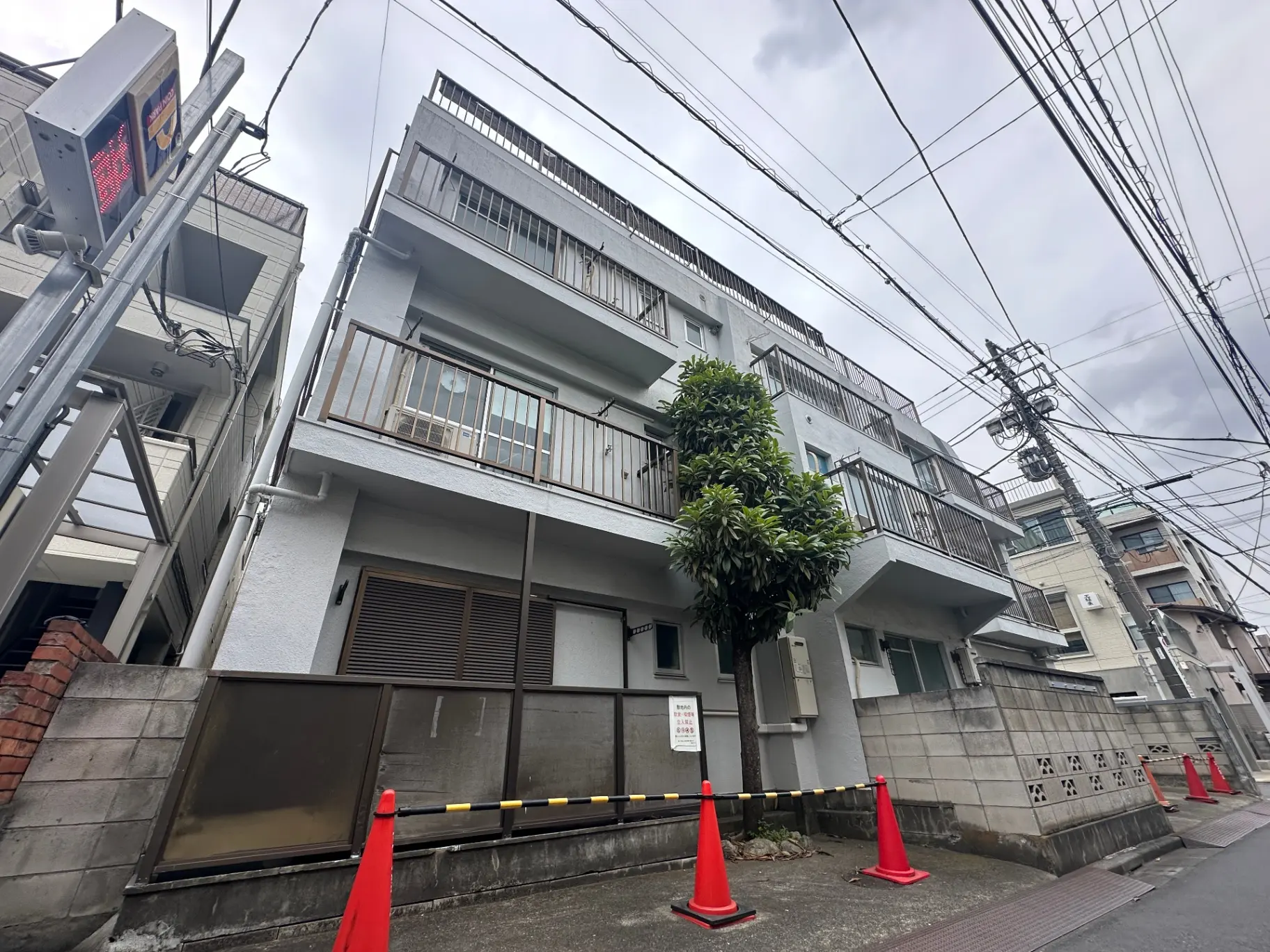 都会のアパート建物、電線が張り巡らされた景色、植栽があるバルコニー