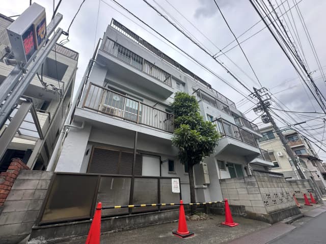 都会のアパート建物、電線が張り巡らされた景色、植栽があるバルコニー