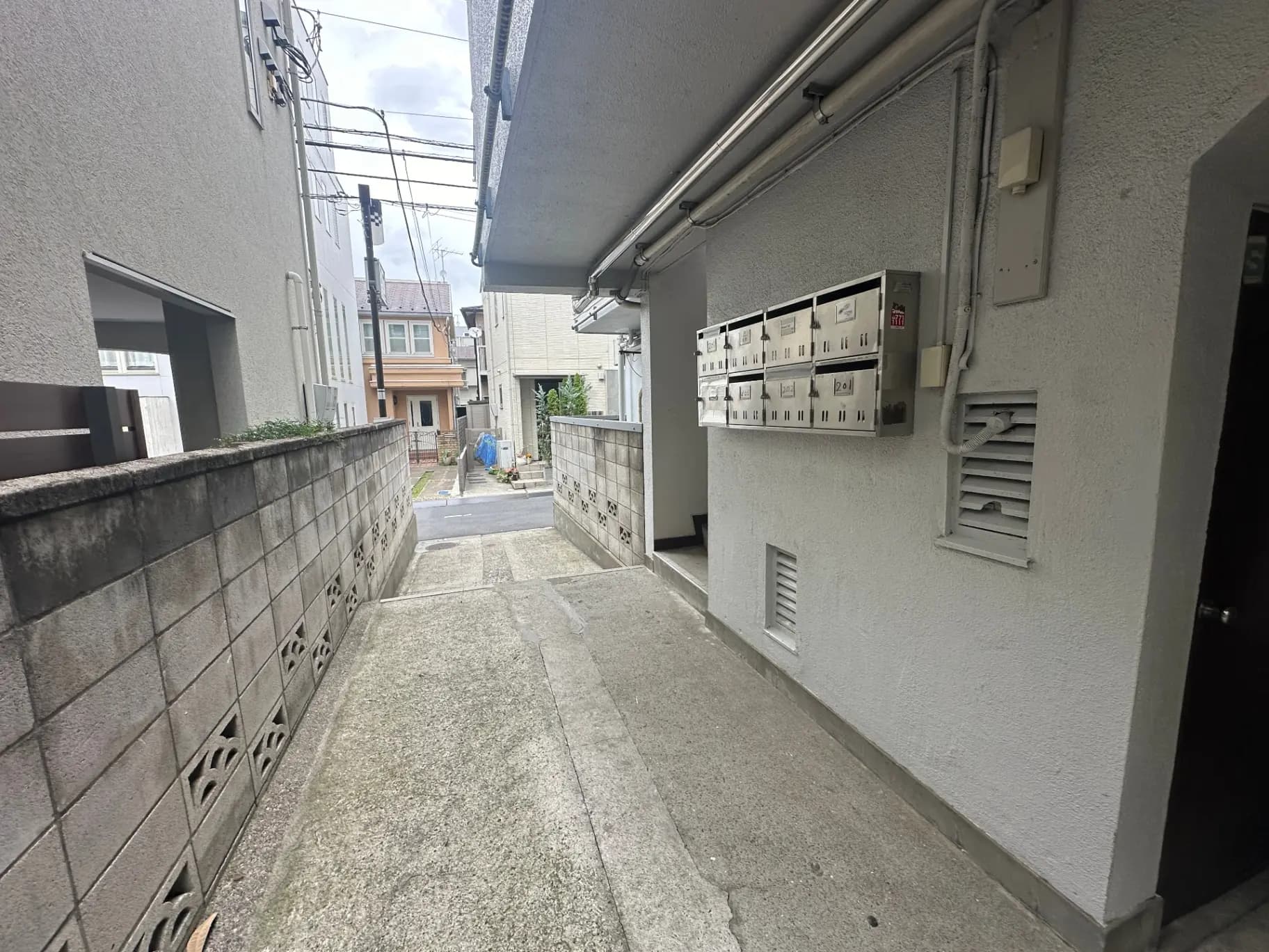狭い通りに沿ったマンションのエントランス、壁に取り付けられた郵便受けと配電盤