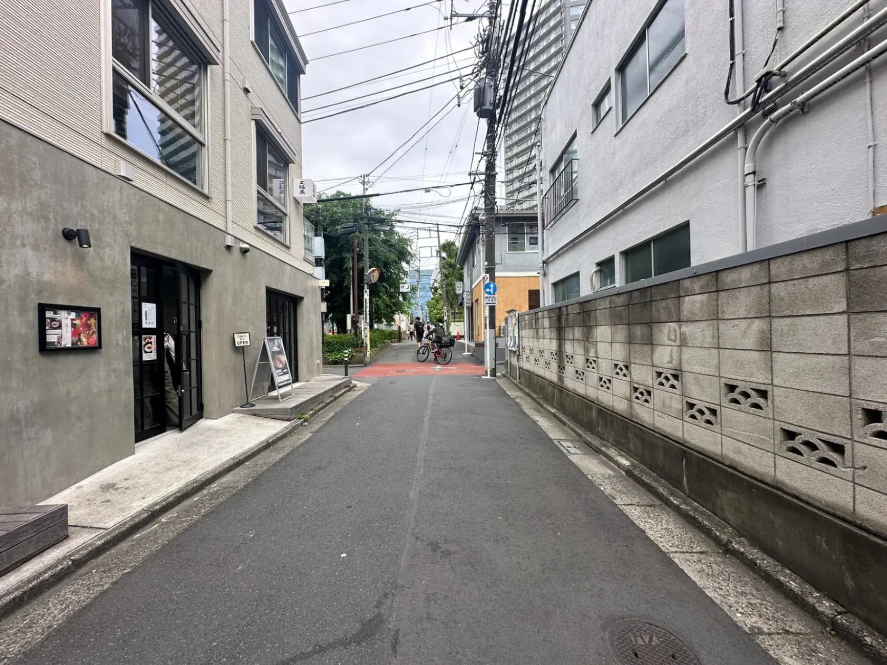 都市の住宅街の狭い道路、自転車に乗る人、コンクリートの建物と緑の樹木