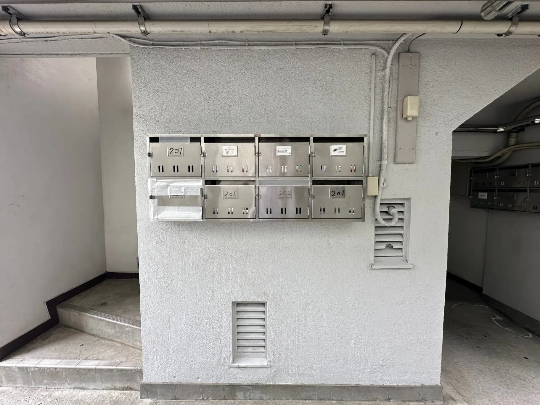 アパートの共用エントランスに設置された郵便受けや表札、建物の管理室の扉が見える写真