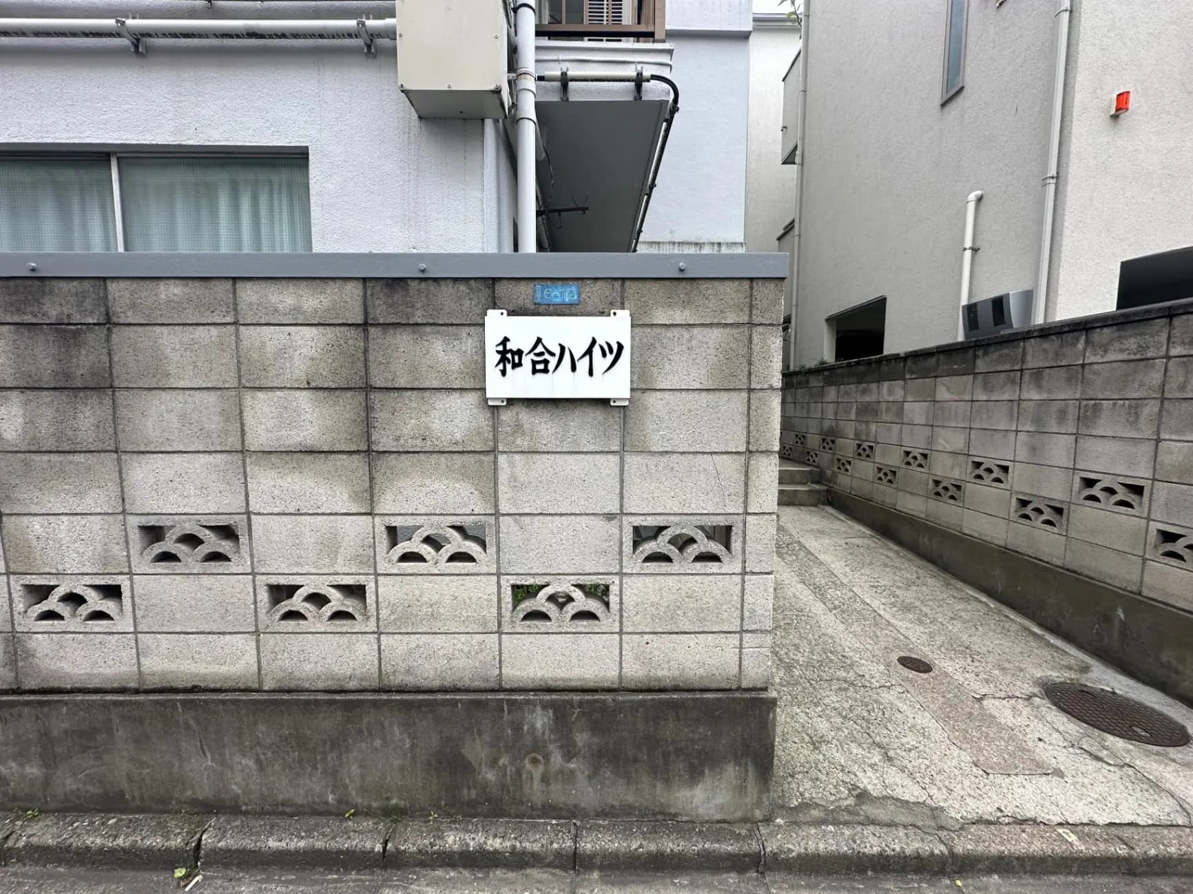 都会の住宅街のコンクリート製の塀と通り、草むらのハローワークの看板