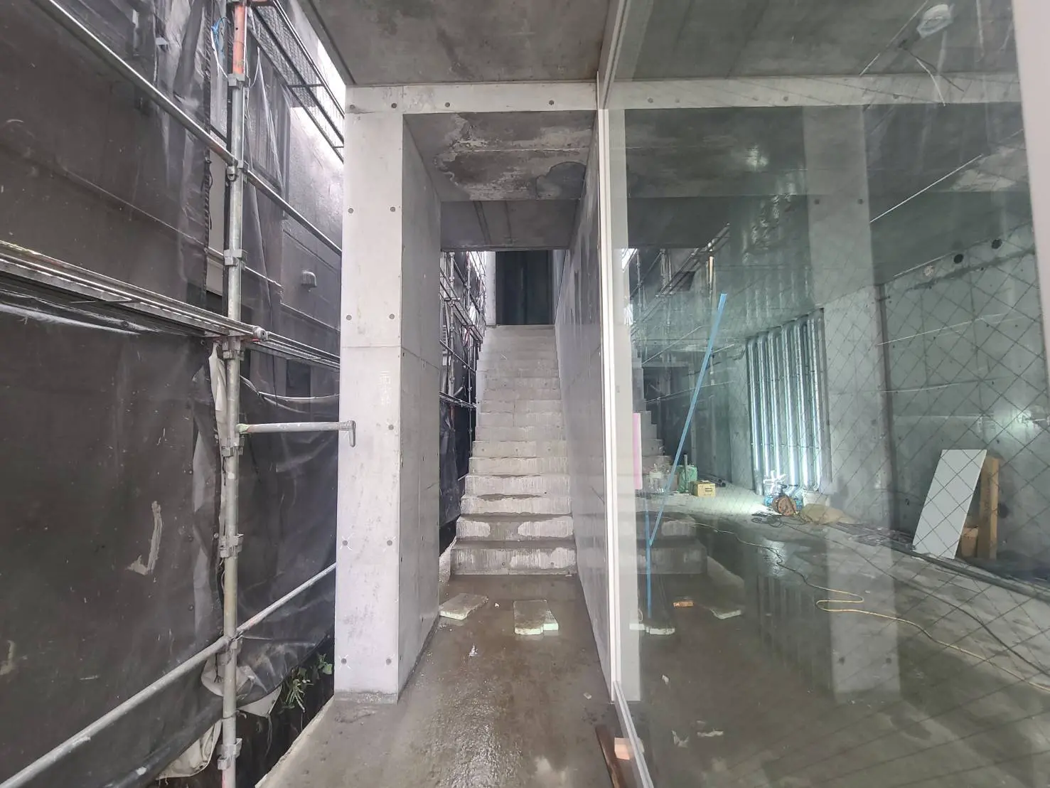 建設中のビルの内部、未完成の階段とコンクリート壁、作業中の保護シートと足場