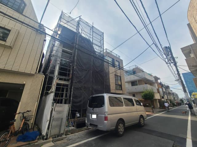 工事中の建物、足場と黒いネット、白いワゴン車、市街地の日常風景