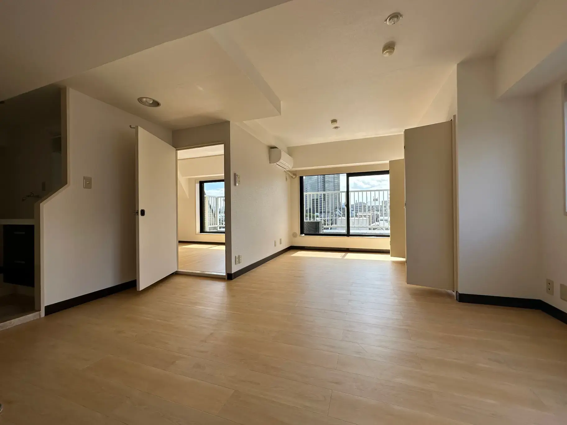 明るい自然光が差し込む木製フロアのリビング、白い壁と大きな窓、シンプルな内装のマンション空間