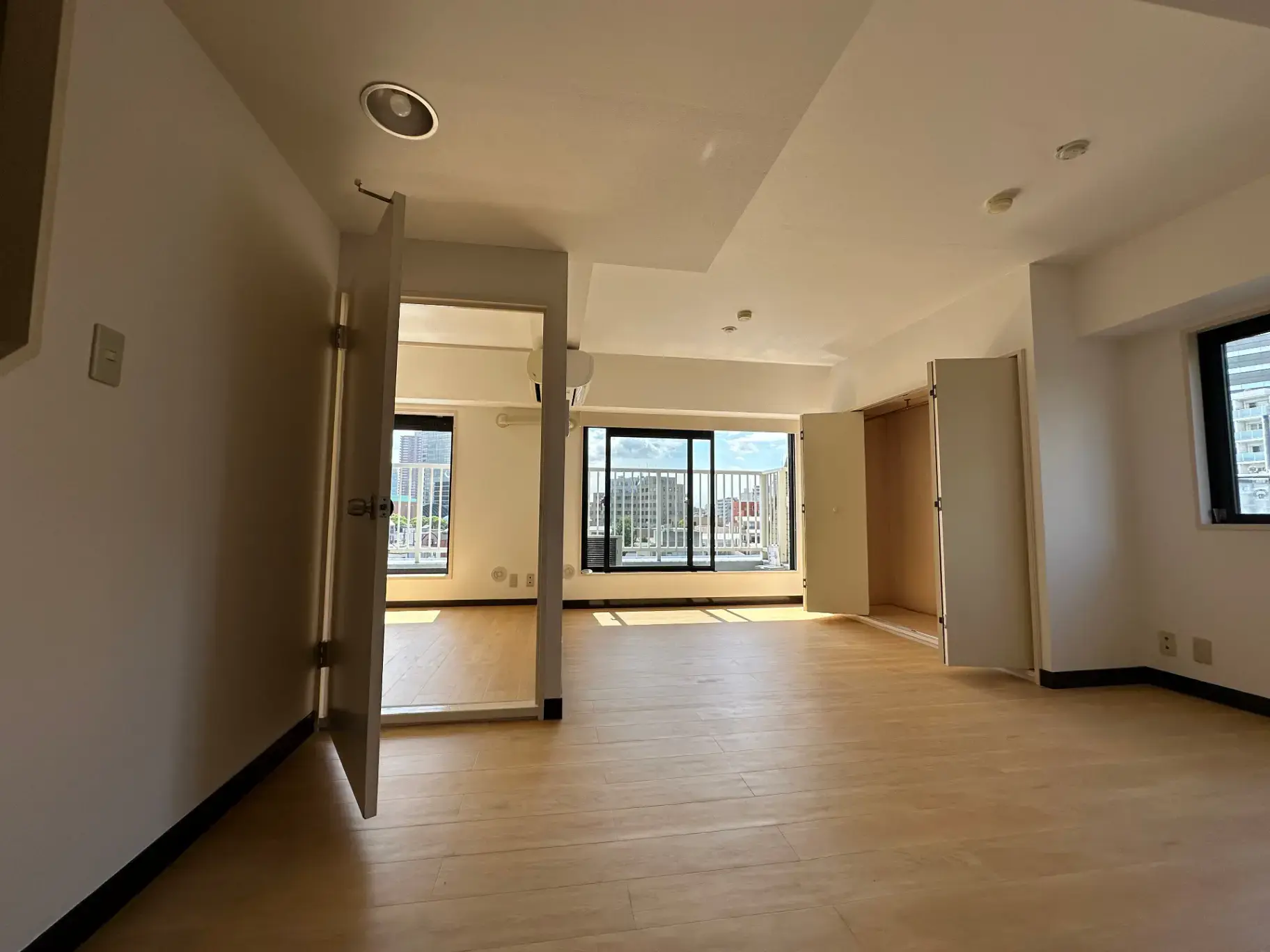 明るい自然光が差し込む広々とした空の部屋、木製フロアと白い壁、開放的な窓とシンプルな内装