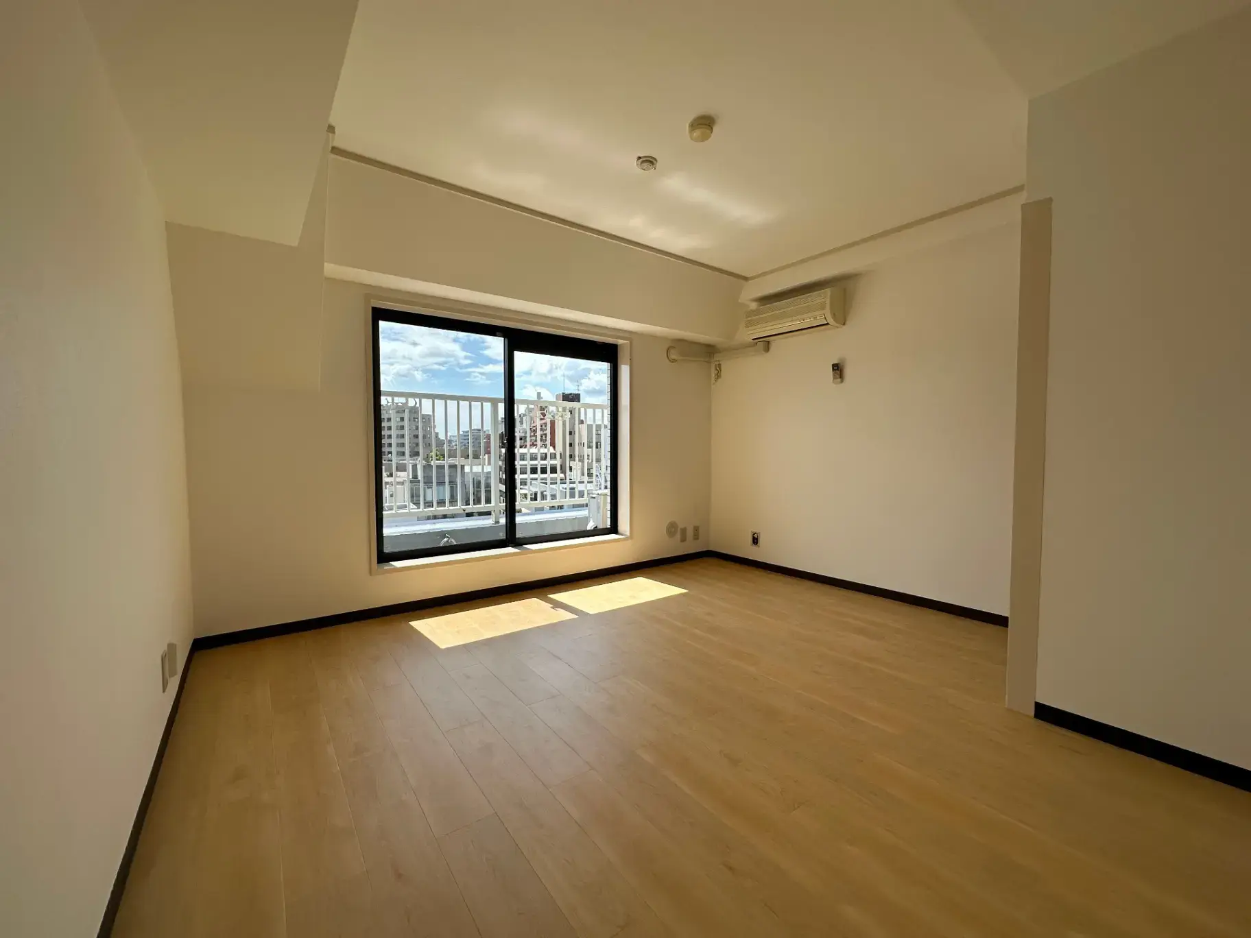 明るい自然光が差し込む空の部屋、木製フローリング、大きな窓、シンプルなインテリアデザイン