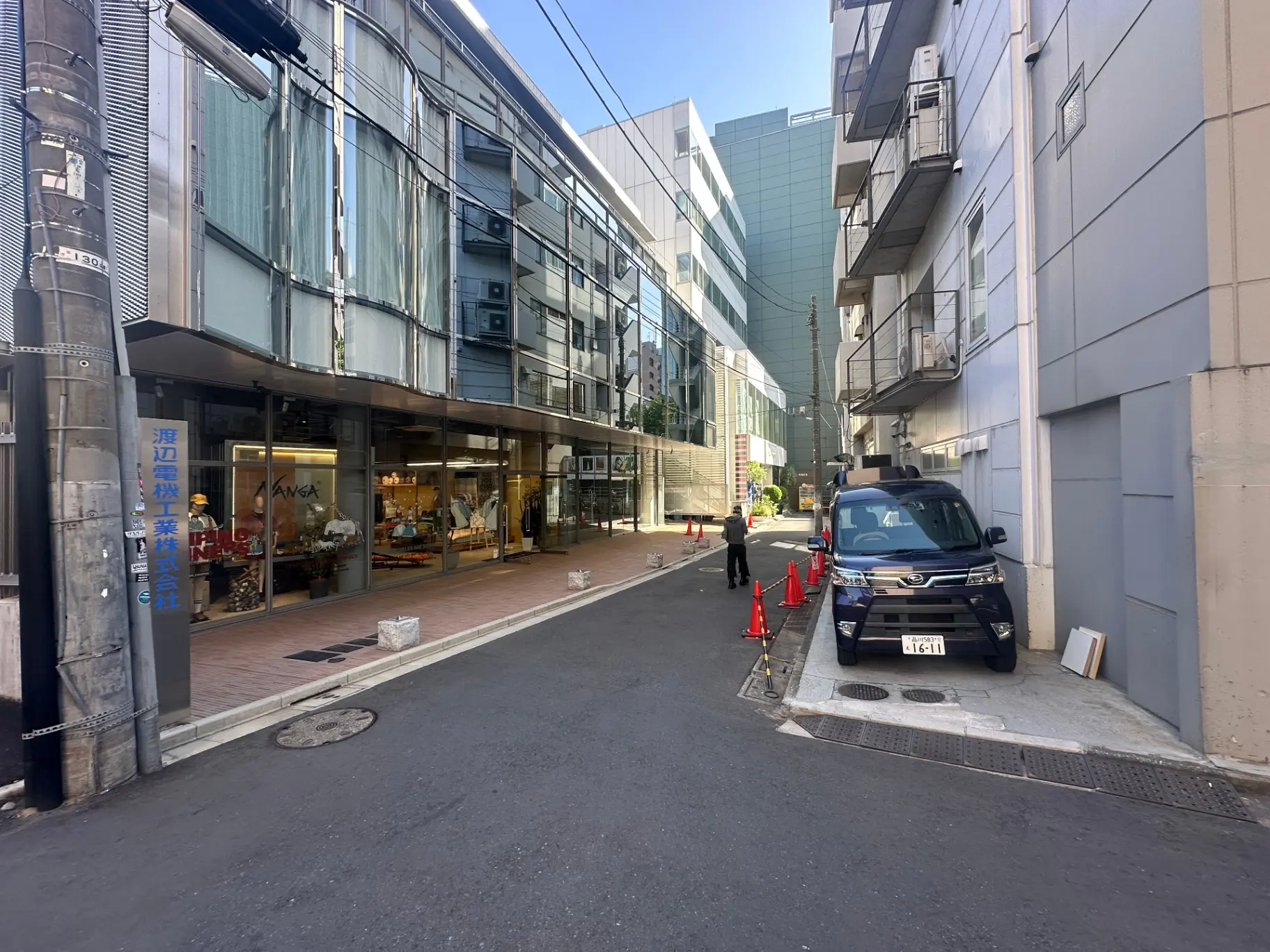 都会の路地裏にあるファッションショップ、ガラス張りのファサード、駐車車両と歩行者の様子