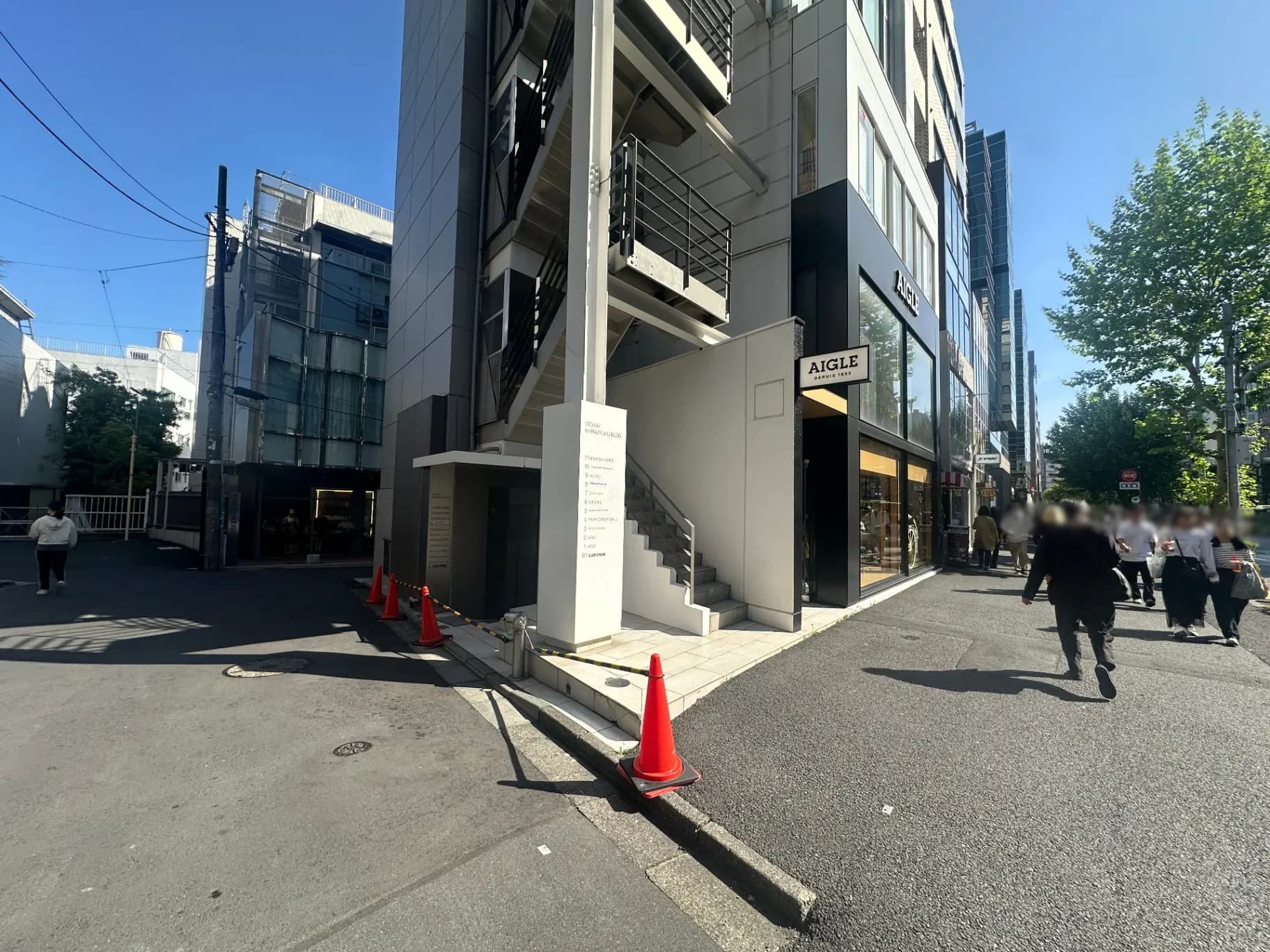 都会の通りにあるAIGLEの店舗、通行人が歩く歩道、朝日が照らす建物と清潔感のある外観