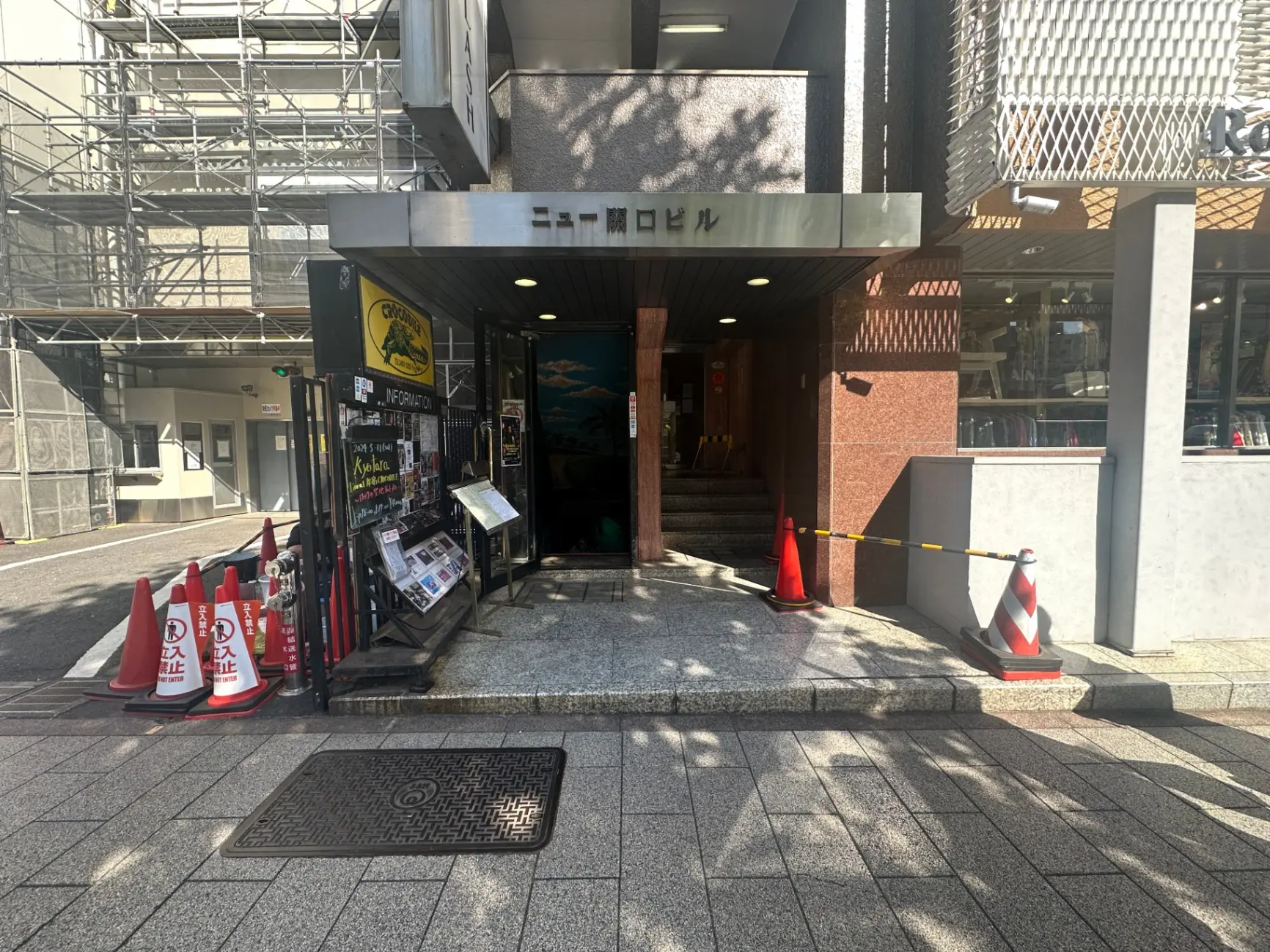 工事中のビルの足場とコンクリートの入り口、黒い看板に黄色の文字で「インフォメーション」表示