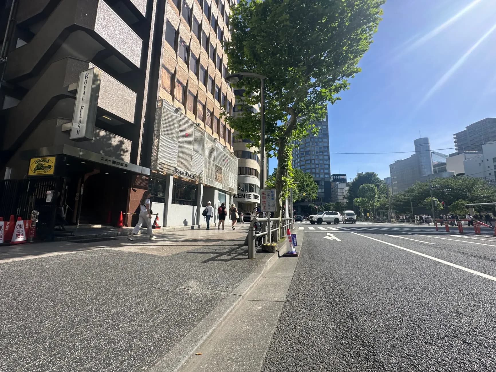 都心のビル街の通り、日差しが差し込む歩道、建物の入り口には看板が掲げられている