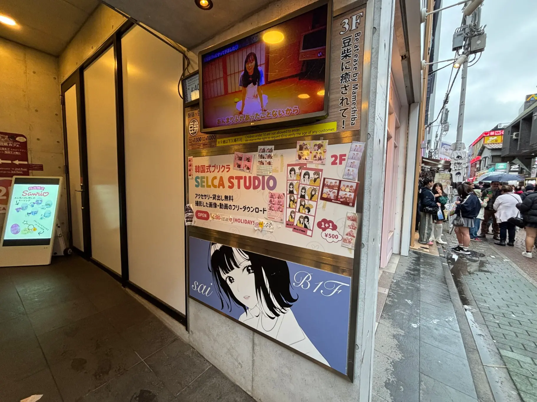 - 原宿にある韓国式セルカスタジオの外観、明るい看板と行列する客たちの様子、背景には街の風景が広がる