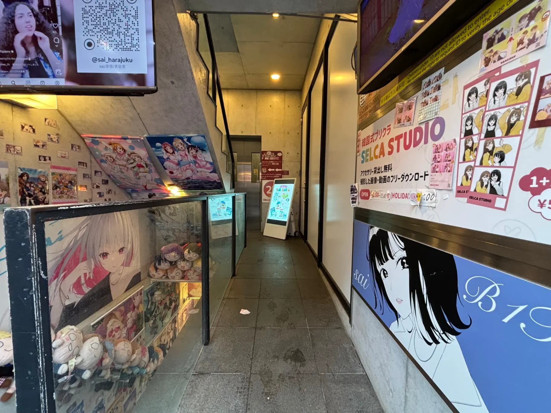 - ハラジュクのセルカスタジオ入口、アニメ風のポスターやキャラクターが飾られた壁、可愛いぬいぐるみが並ぶガラスケースのある光景